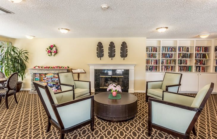 A cozy living room with armchairs around a coffee table, featuring a fireplace and bookshelves.