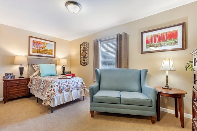 A cozy bedroom with a single bed and a small couch, complemented by wall art and warm lighting.