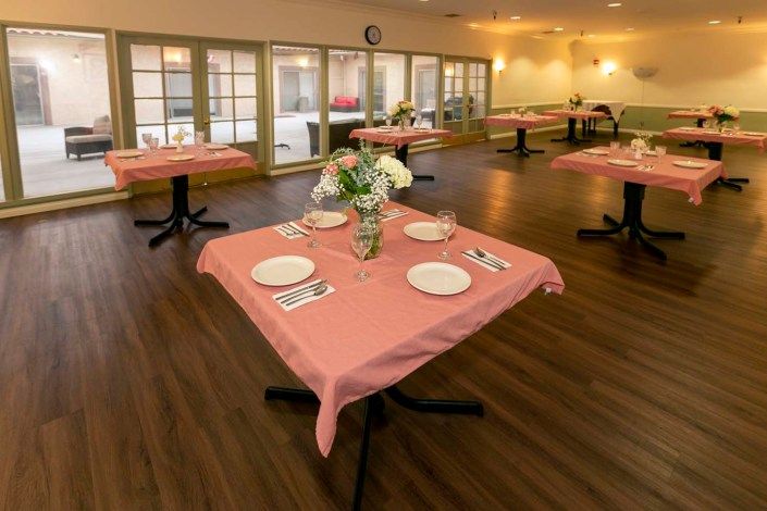 A neatly arranged dining area with tables set for service, featuring pink tablecloths and floral centerpieces.