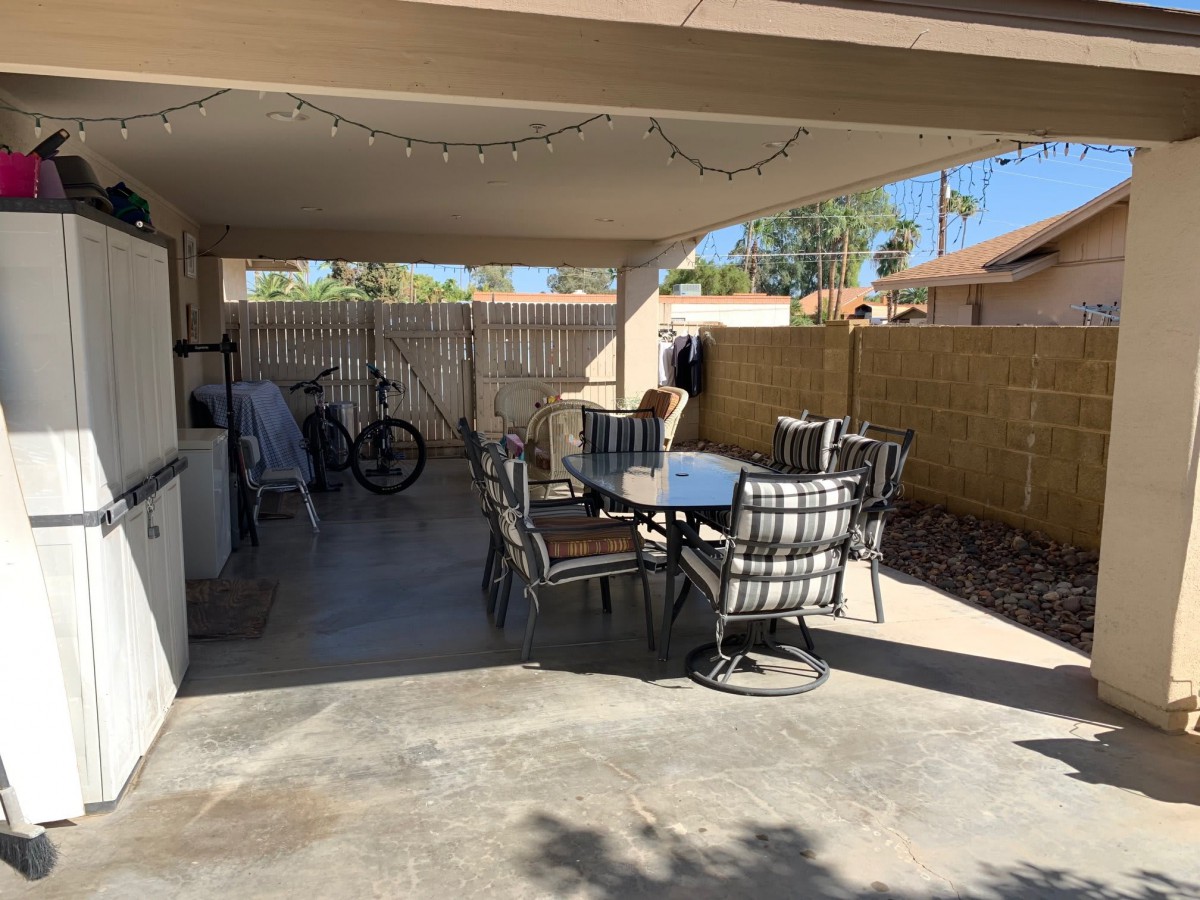 A cozy covered patio area featuring a table with chairs, a bicycle, and outdoor decor.