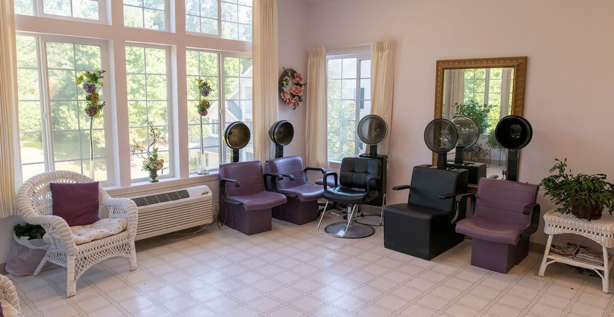 A salon interior featuring multiple chairs and hair dryers next to large windows.
