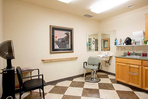 A small hair salon with a chair, mirror, and artwork on the wall.