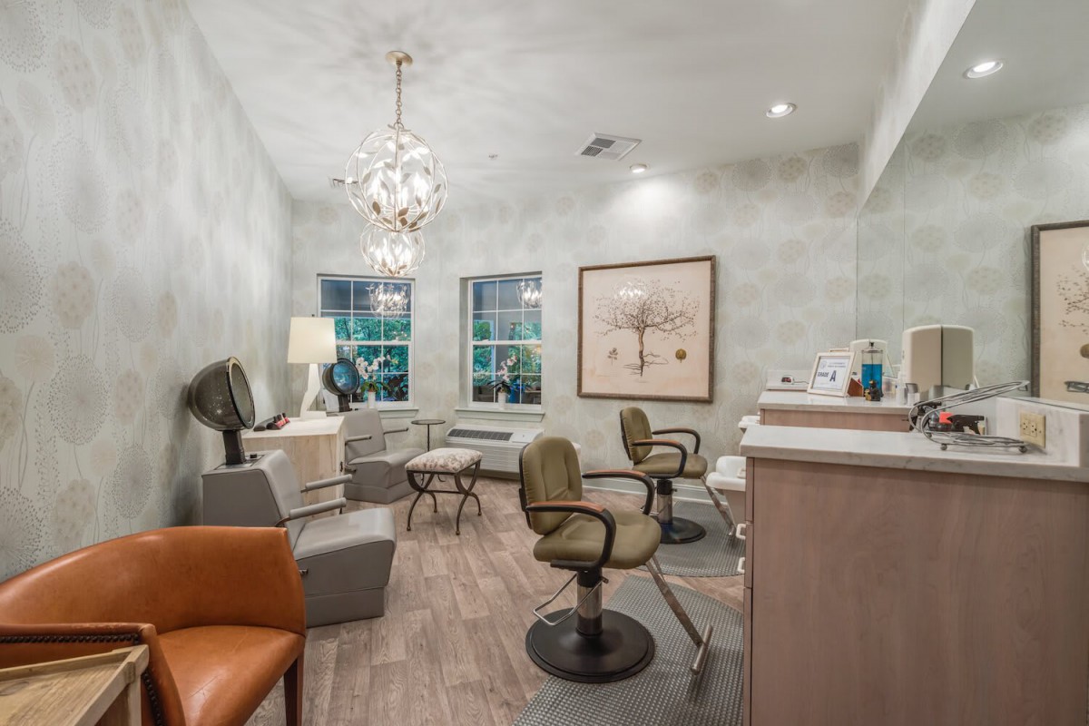 A stylish salon interior featuring comfortable seating, a chandelier, and modern decor.