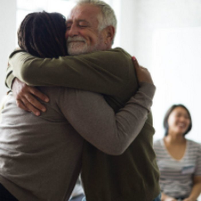 Two people sharing a warm hug while another person smiles in the background.