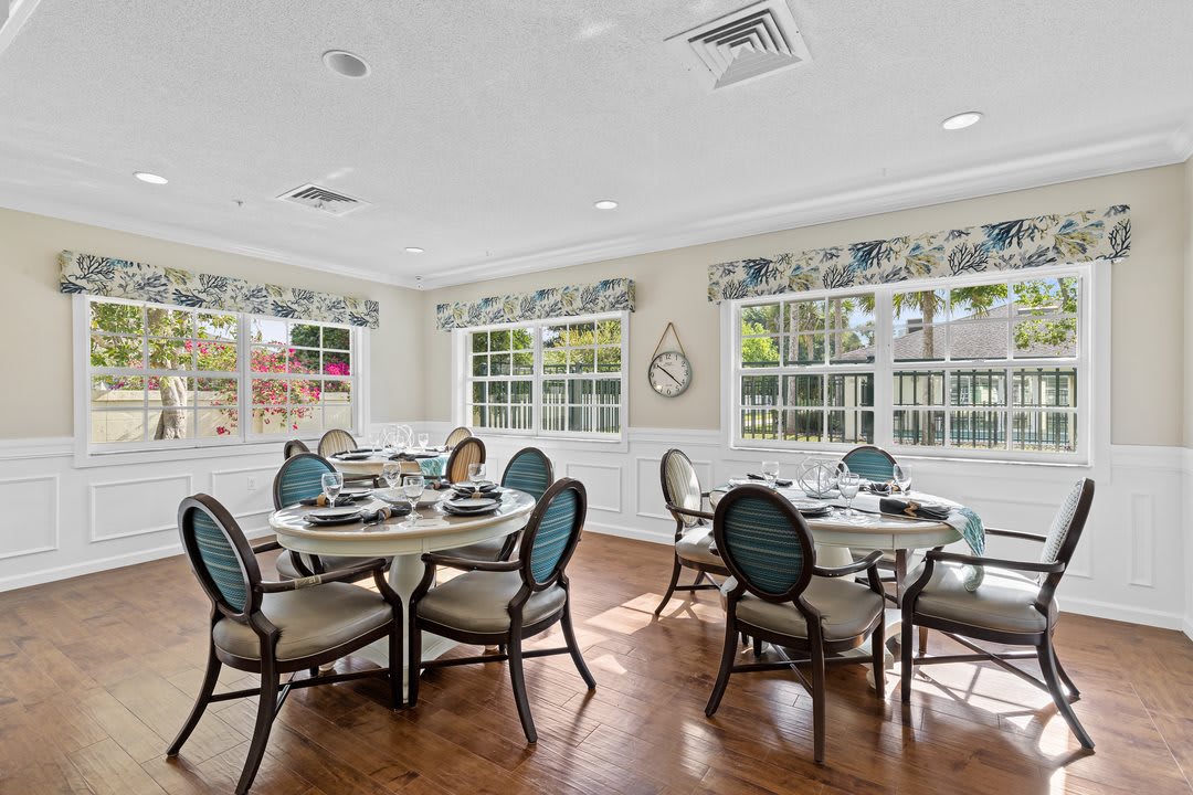 A well-lit dining room with multiple tables and chairs, featuring large windows and elegant decor.