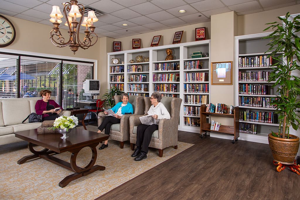 A cozy library setting with people sitting and reading in comfortable chairs surrounded by bookshelves.