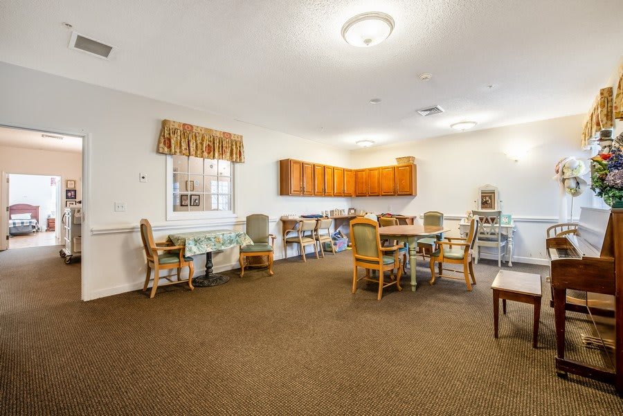 A dining area with tables and chairs, featuring wood cabinets and carpeted flooring.