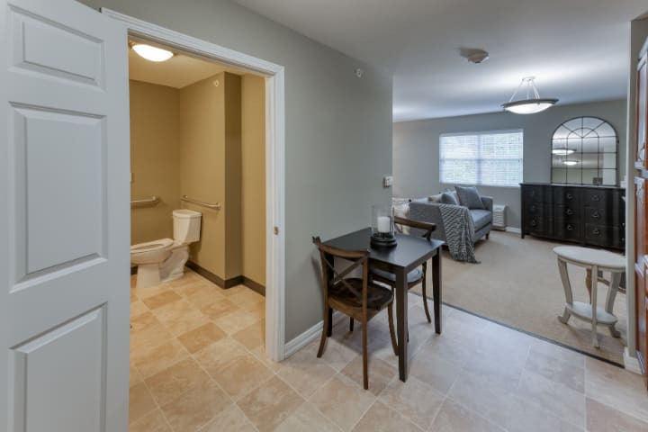 A cozy apartment interior featuring a small dining area, adjacent bathroom, and a living room.