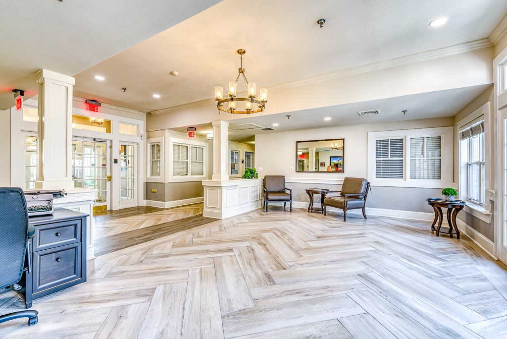A bright and spacious lobby area featuring elegant furniture, a chandelier, and a patterned hardwood floor.