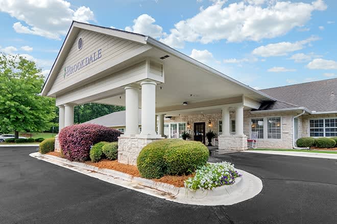 The entrance of a building with landscaped shrubs and a paved driveway.