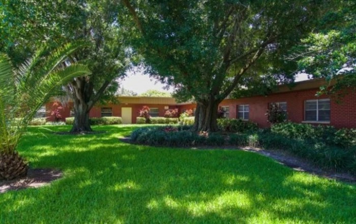 A quaint brick house surrounded by lush green grass and large trees.
