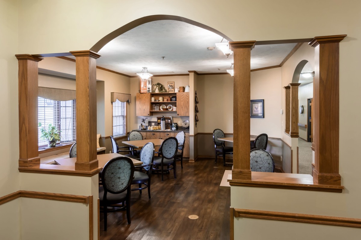 A cozy dining area with a view into an adjoining kitchen, featuring traditional decor and wooden furniture.