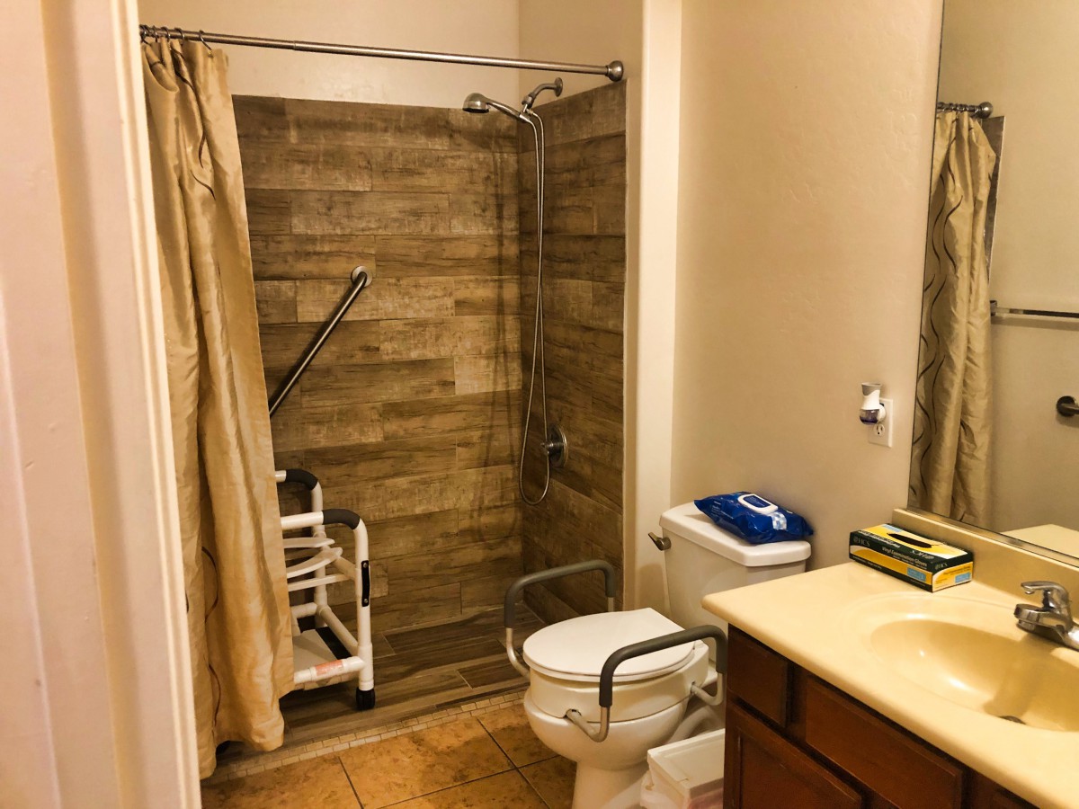 An accessible bathroom with a shower area, equipped with grab bars and a shower chair.
