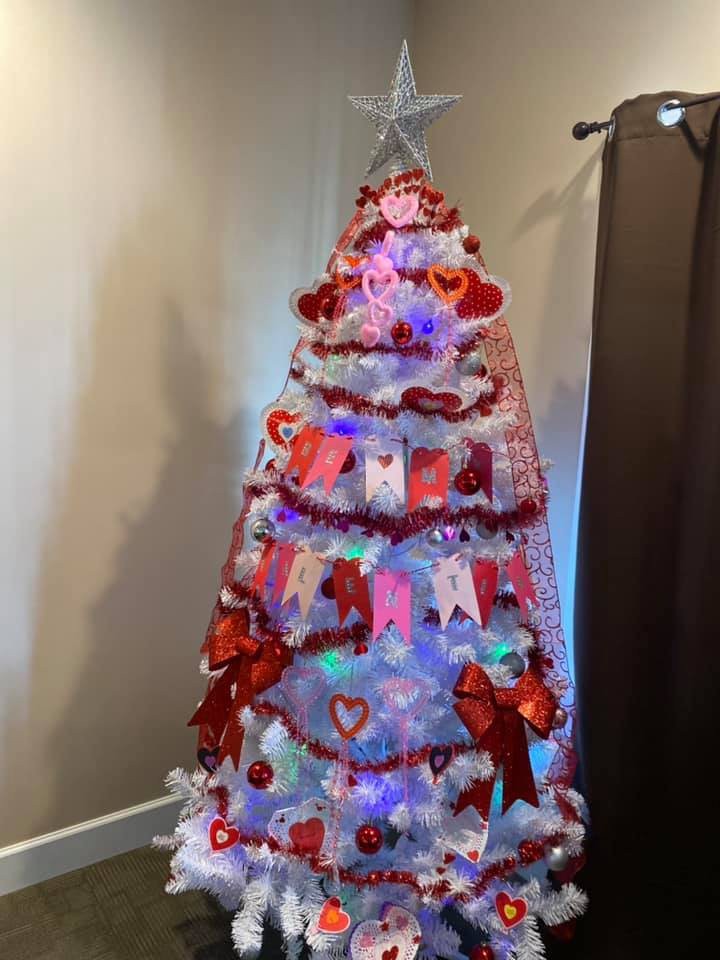 A festive Christmas tree adorned with red and white decorations, including hearts, bows, and lights.