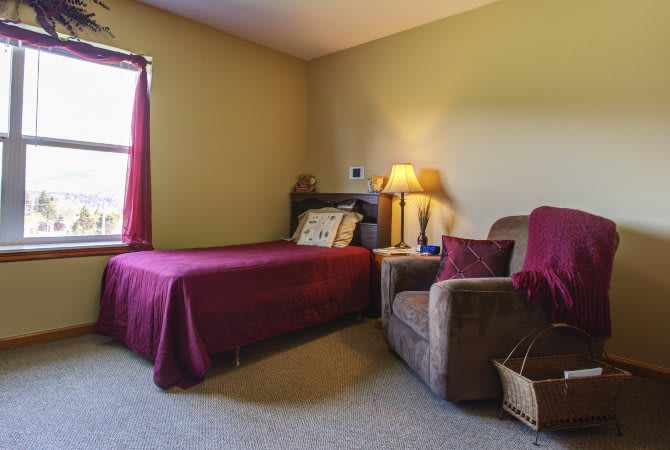 A cozy bedroom with a single bed, armchair, and soft lighting from a lamp by the window.