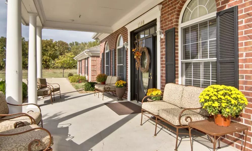 A cozy porch with outdoor seating and floral decorations at the entrance of a brick house.