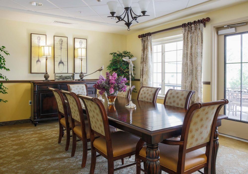 A well-decorated dining room featuring a large table, elegant chairs, a chandelier, and a window with curtains.