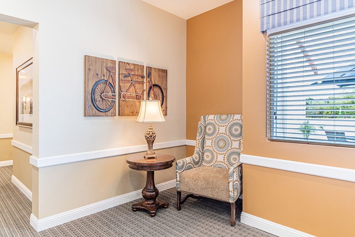 A cozy corner featuring an armchair, a table with a lamp, and artwork on the wall.
