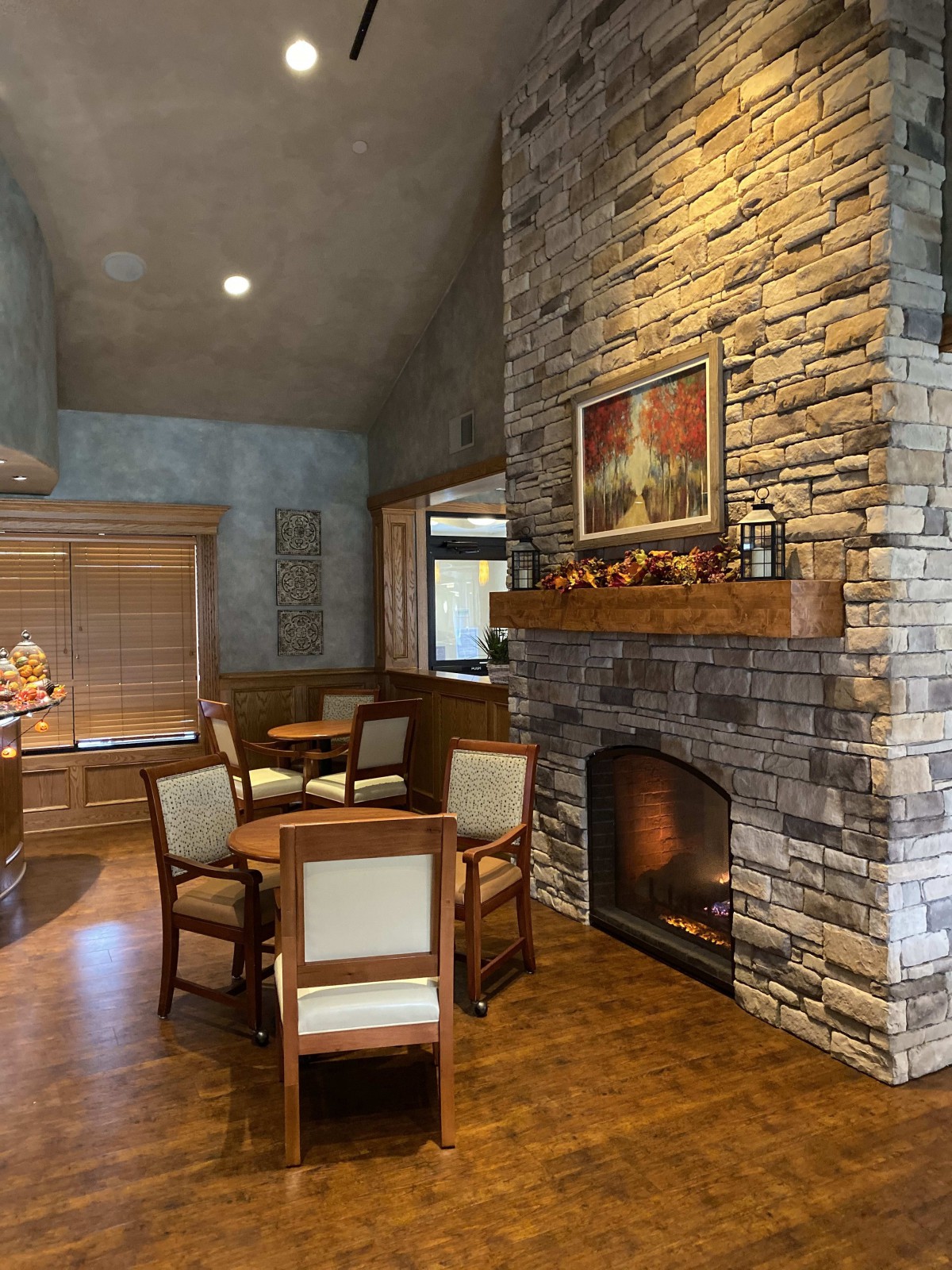 A cozy living room with a stone fireplace, wooden furniture, and a painting above the mantel.
