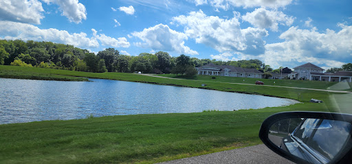 A serene view of a lake surrounded by lush greenery and a blue sky filled with clouds.