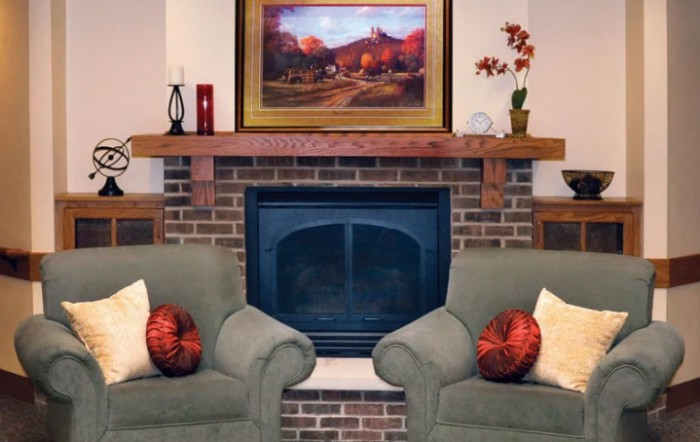 A cozy living room with a brick fireplace, armchairs, and decorative elements.