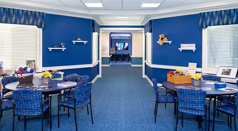 A brightly lit room with blue walls, decorated with shelves and toys, featuring tables and chairs set on a carpeted floor.