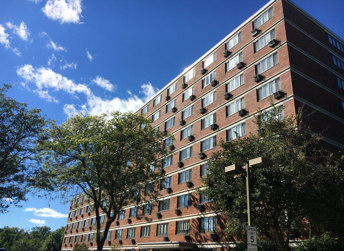 A residential apartment building with a clear blue sky and surrounding trees.