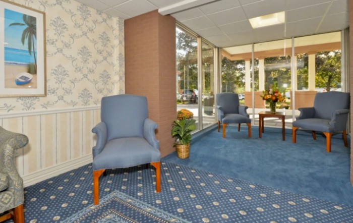 A cozy waiting room with blue upholstered chairs, a patterned carpet, and large windows letting in natural light.