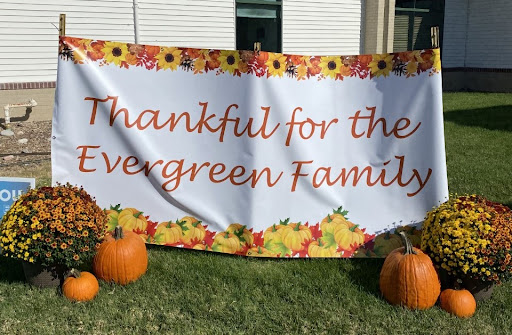 A festive banner expressing gratitude for the Evergreen Family, adorned with autumn leaves and pumpkins.