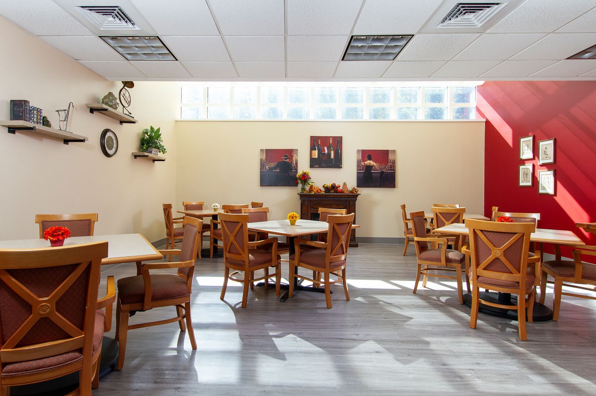 A cozy cafe interior with wooden tables and chairs, decorated with wall art and plants under natural lighting.