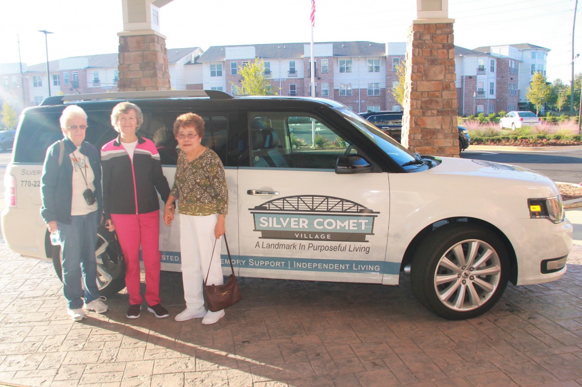 Two people standing in front of a car with a 'Silver Connect' logo, outside a building.