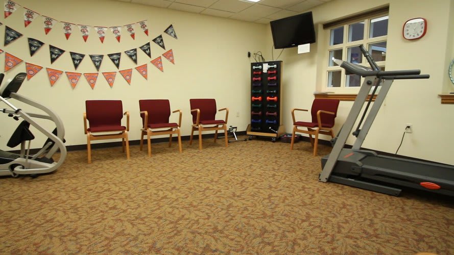 An empty waiting room with chairs, a TV screen, and a treadmill.