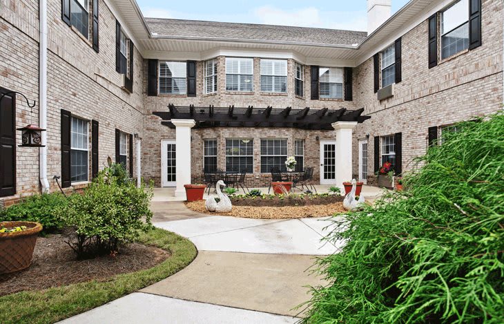 A landscaped courtyard with a pathway surrounded by shrubs and a two-story brick building.