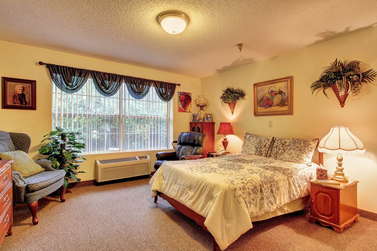 A cozy bedroom decorated with warm tones and featuring a large window, a bed with patterned bedding, and various decorative elements.