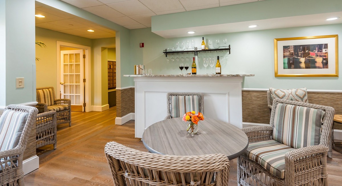 A cozy home bar setup in the basement with a small round table, wicker chairs, and wine displayed on the counter.