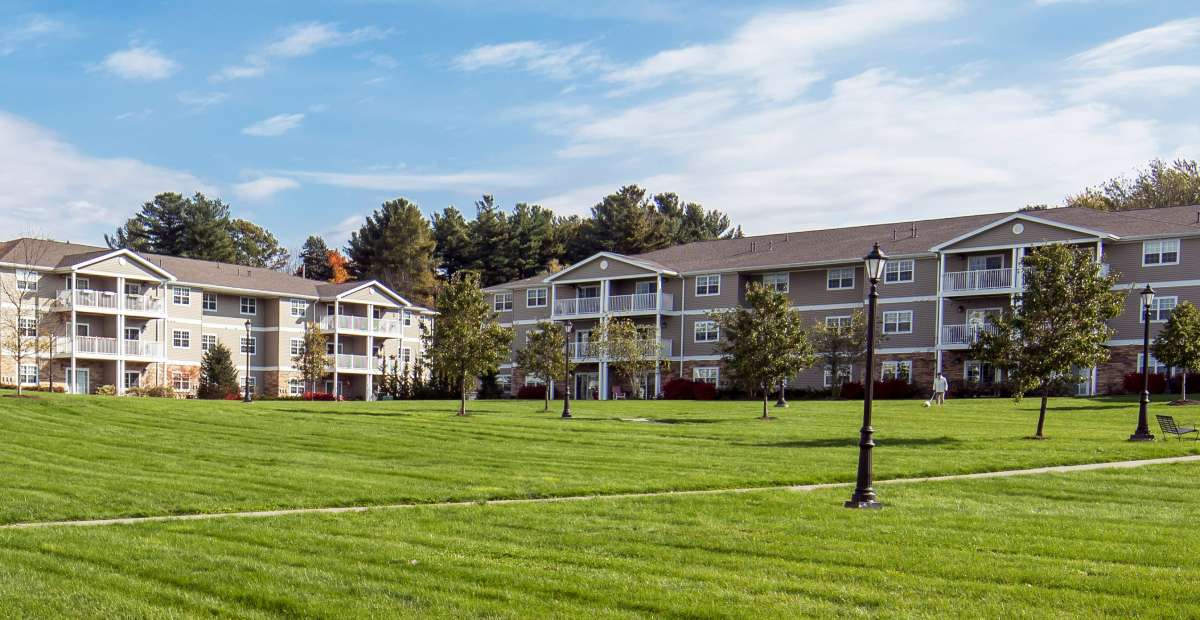 A modern apartment building with a spacious green lawn and surrounding trees.