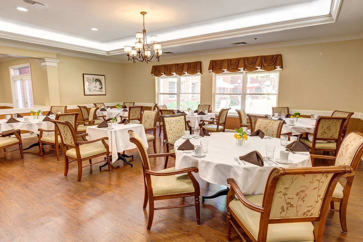 An elegant dining room with neatly arranged tables and chairs, featuring chandeliers and large windows.