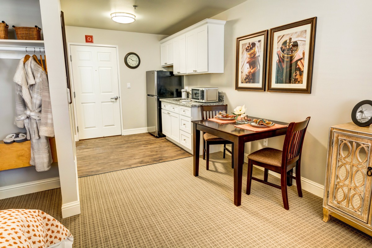 A modern kitchen and dining area featuring a compact kitchenette, a wooden table with two chairs, and framed artwork on the walls.