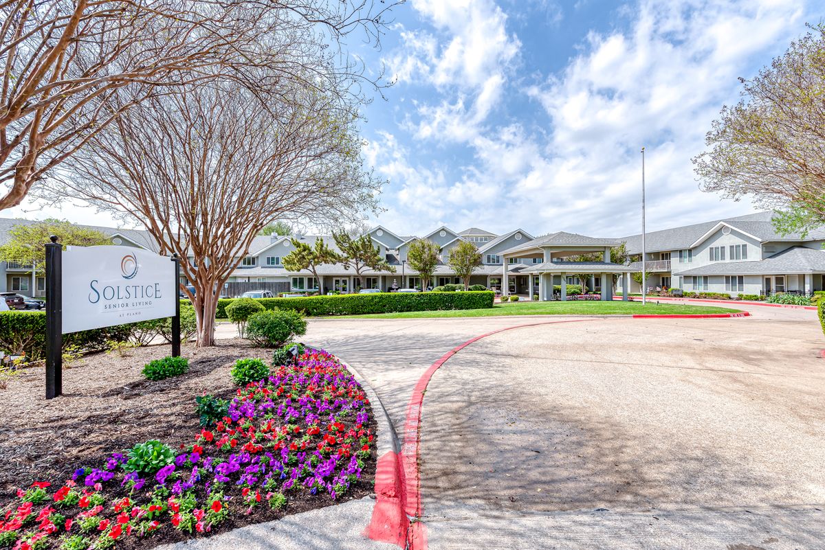 A landscaped garden with colorful flowers leads to a large building under a partly cloudy sky.