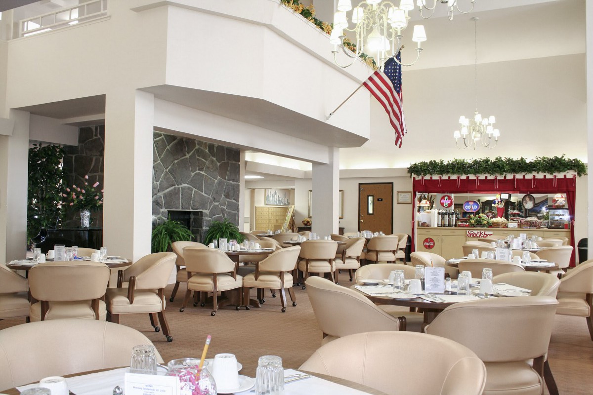 A well-lit dining area with neatly arranged tables and chairs, featuring an American flag and elegant decor.