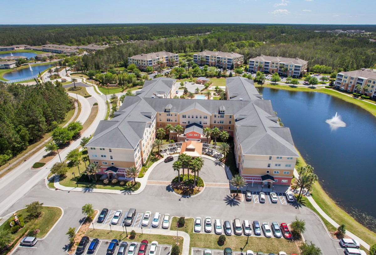 Aerial view of a residential apartment complex with a central lake and surrounding parking areas.