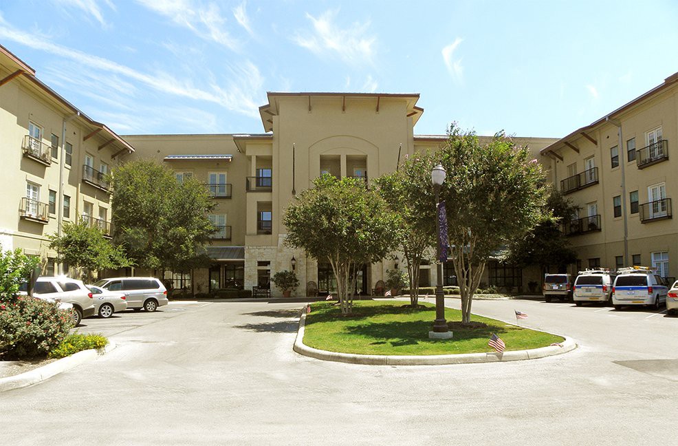 A residential building with a parking area and trees in front, captured on a sunny day.