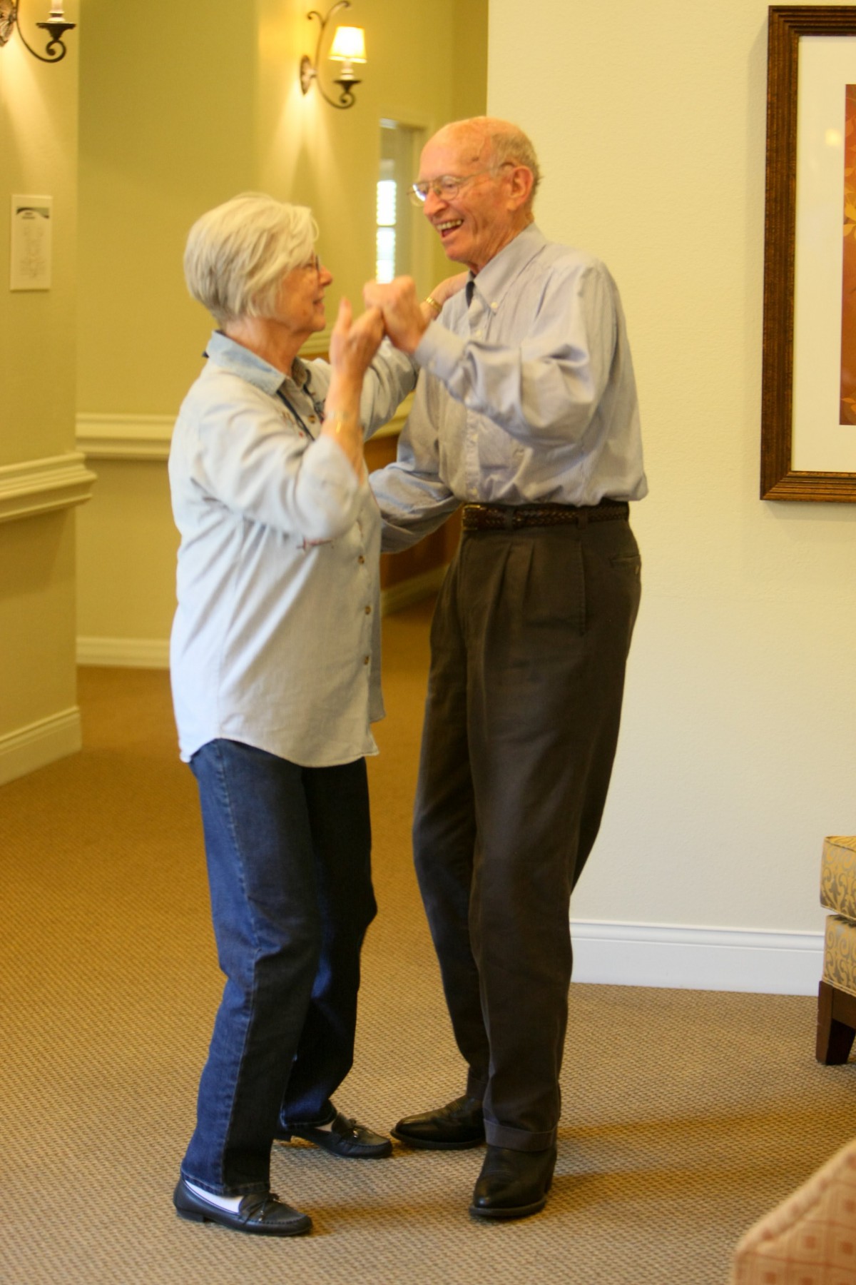An elderly couple dancing together indoors, enjoying a moment of leisure.