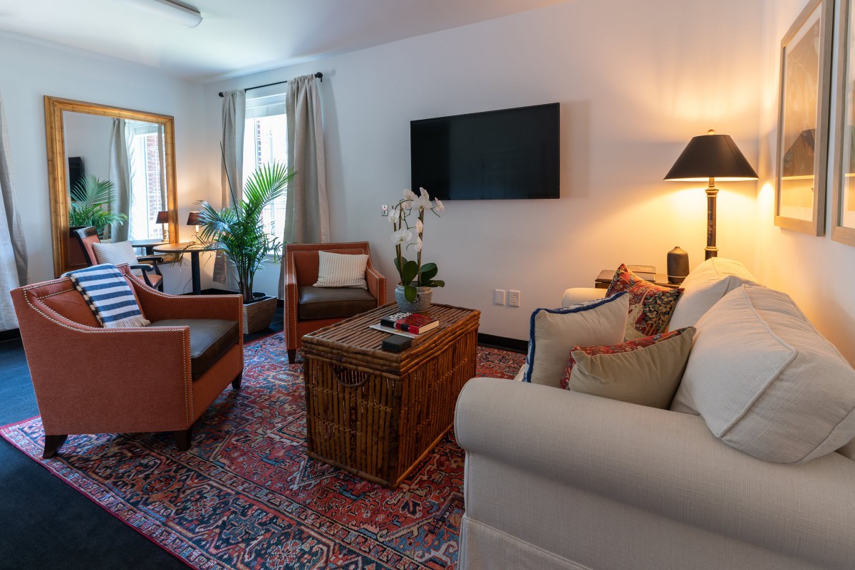 A cozy living room with modern decor, featuring a comfortable sofa, armchairs, a woven coffee table, and a large TV mounted on the wall.