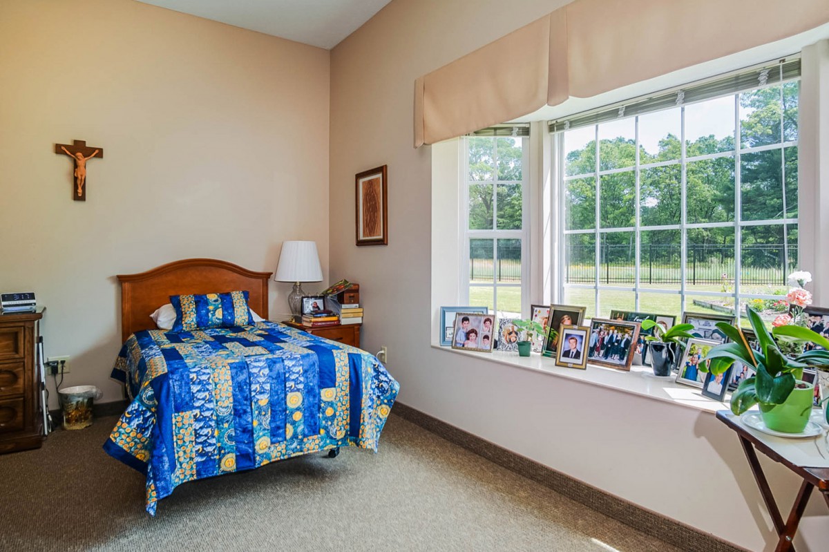 A cozy bedroom with a single bed featuring colorful bedding, a window seat adorned with decorative items and photos, and soft natural light.