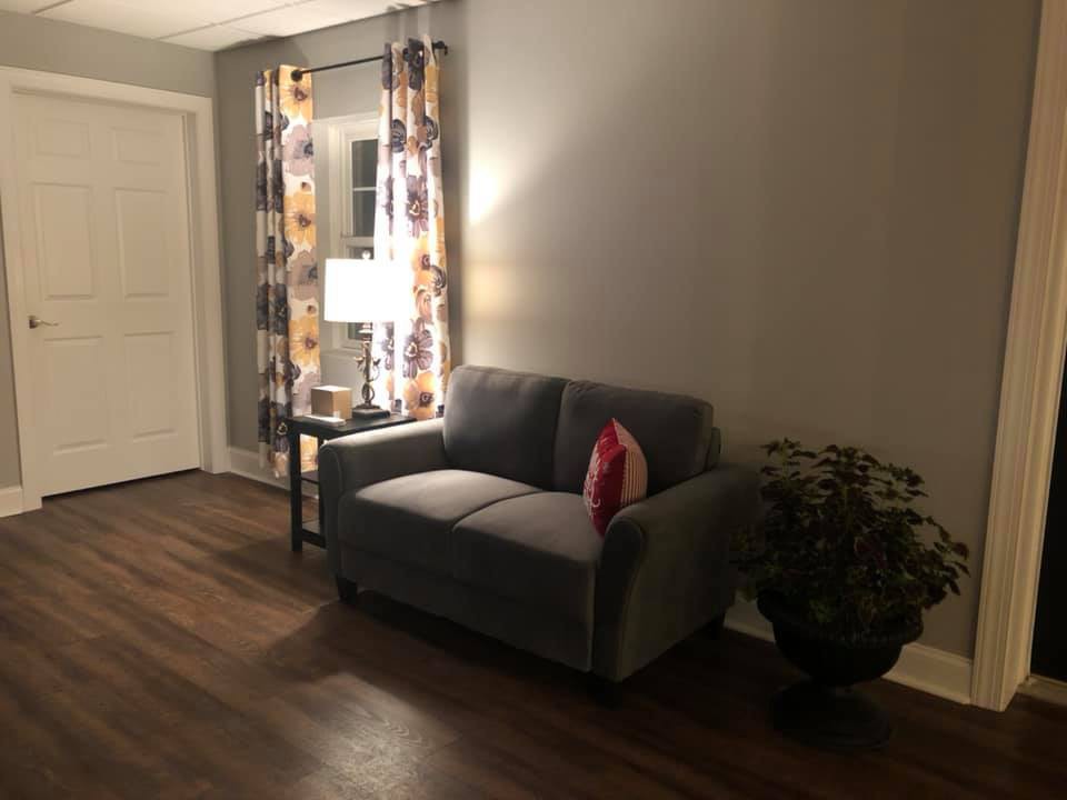 A cozy living room with a small sofa, a lamp on a side table, and decorative plants.
