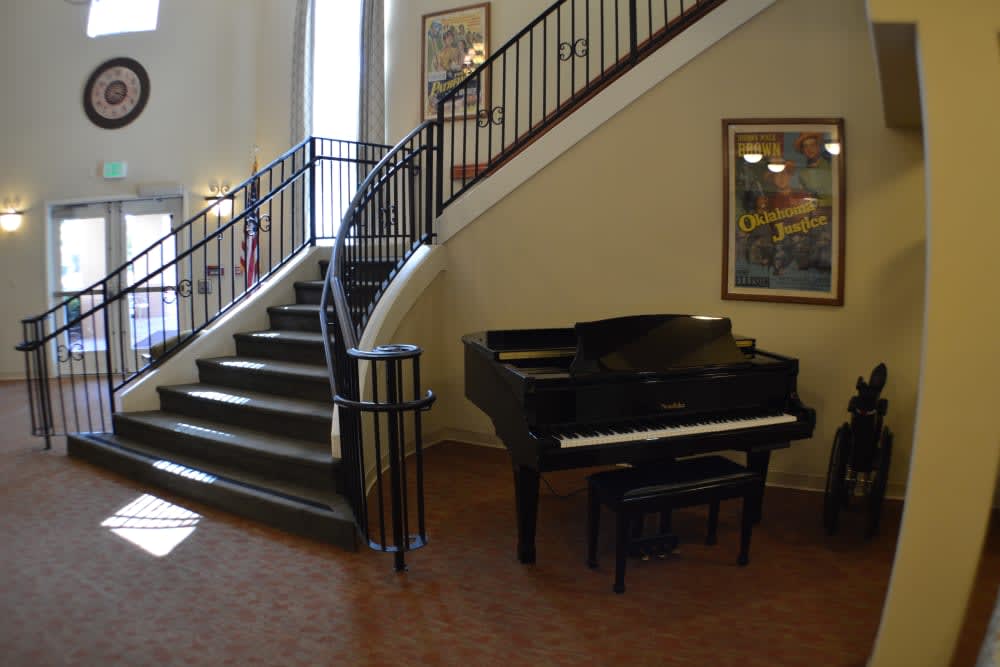 A grand piano sits beside a winding staircase in a well-lit interior space adorned with artwork.