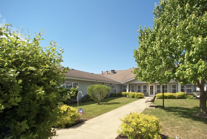 A sunny day view of a house surrounded by well-maintained gardens and trees.