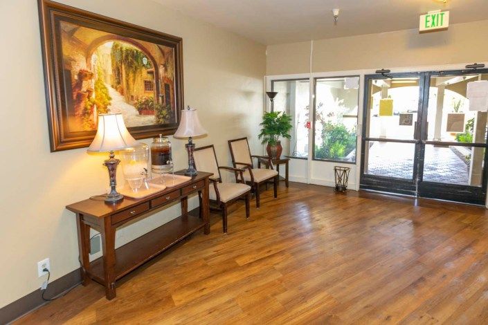 A well-lit lobby area with wooden flooring, featuring chairs, a console table with lamps, and decorative artwork.