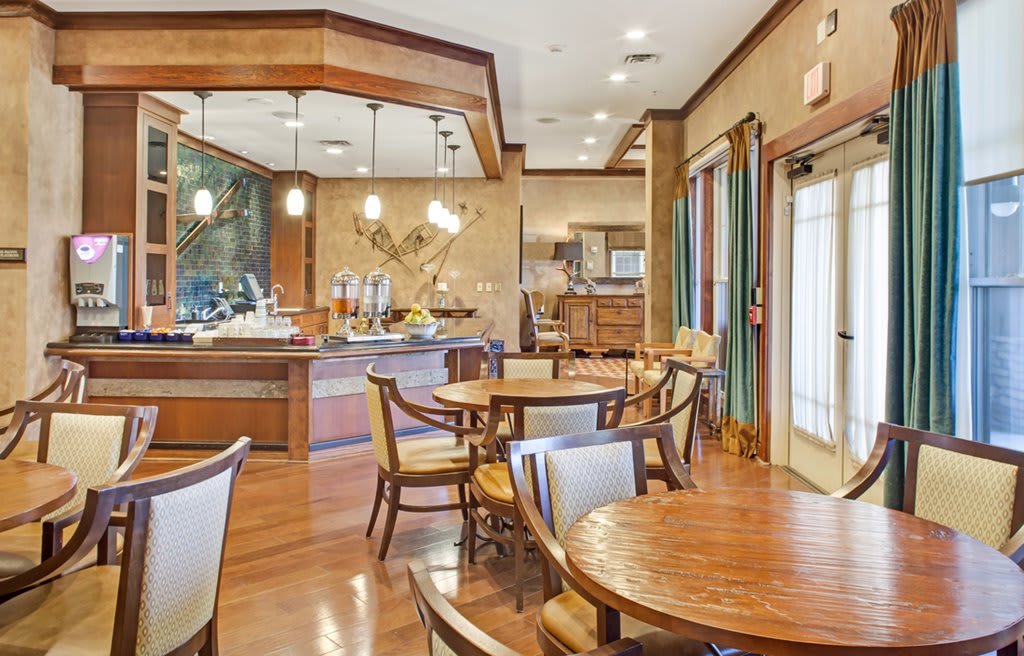 A cozy dining area with wooden tables and chairs, featuring elegant lighting fixtures.